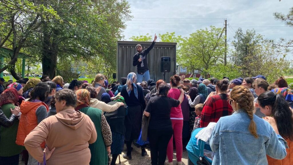 Man sharing to a crowd of Ukrainians while pointing to the sky.