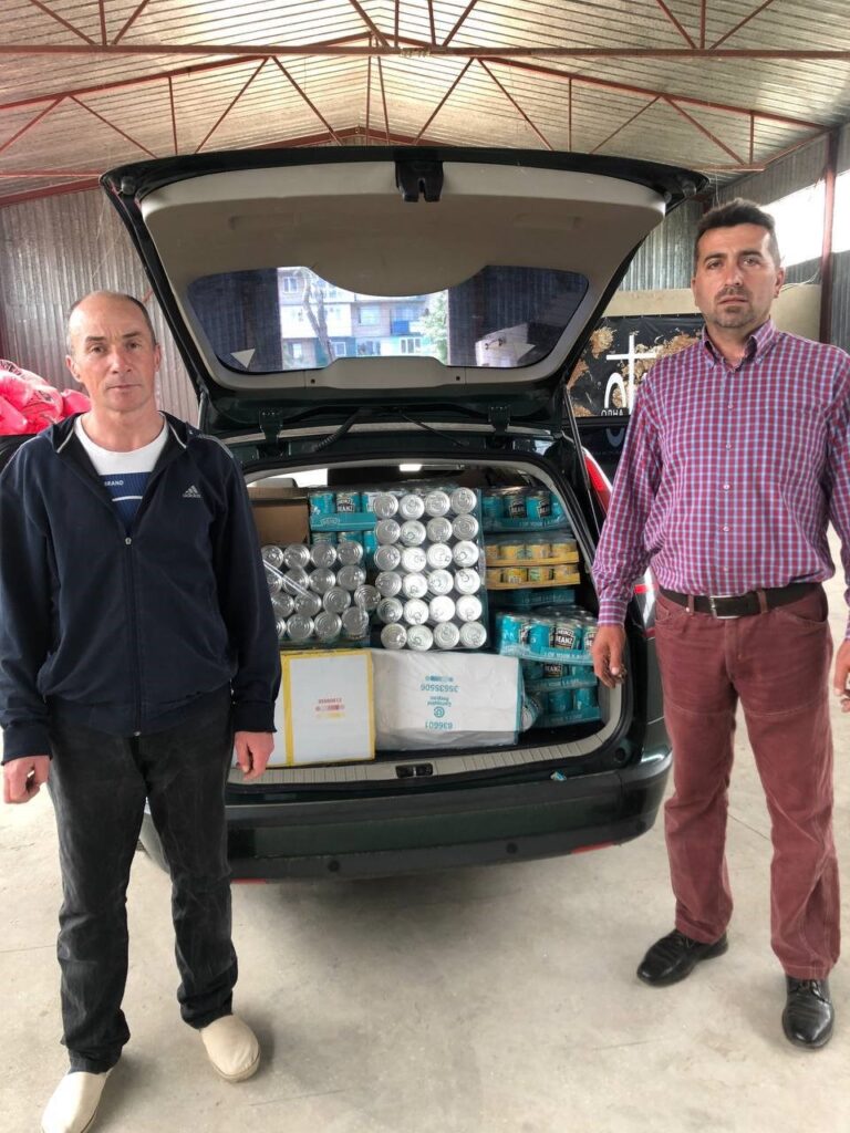 Two men in front a vehicle with supplies.