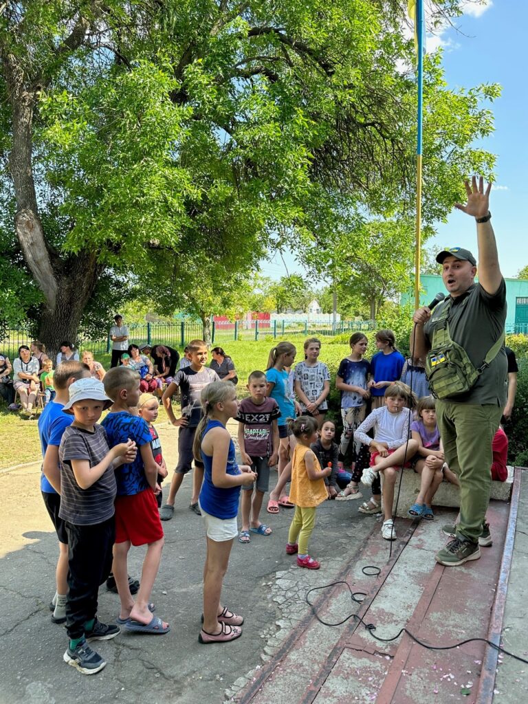 Man holds his hand high in the air and shares a message over the microphone to the kids and adults in attendance.