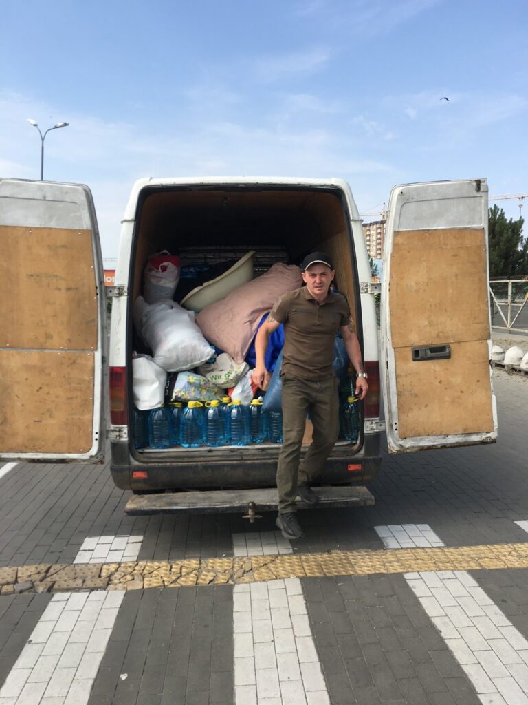 Man in front of van that is filled with food and supplies.