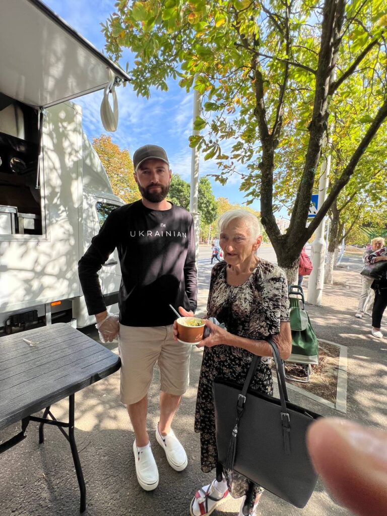 Older lady holding a plate of food, she is standing by a man