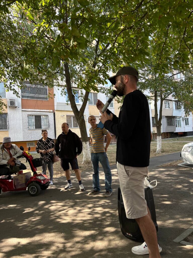man holding mic and preaching to a group of 5 people in the streets