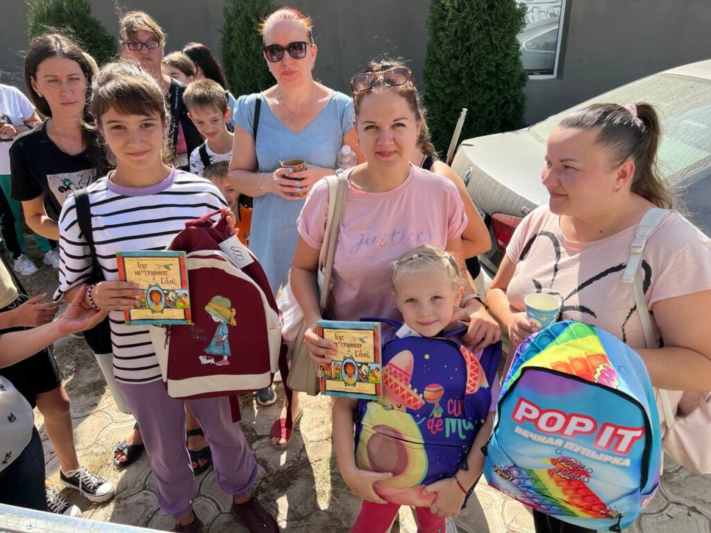 Women and children holding backpacks