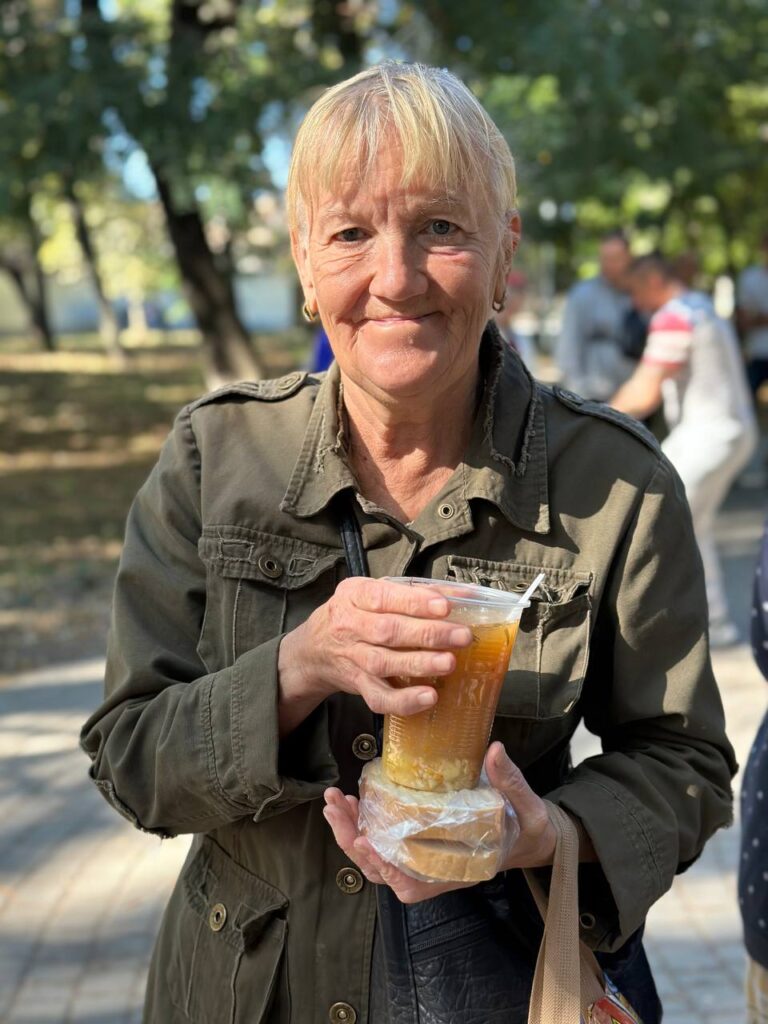 elderly woman holding a cup of warm soup and a sandwich