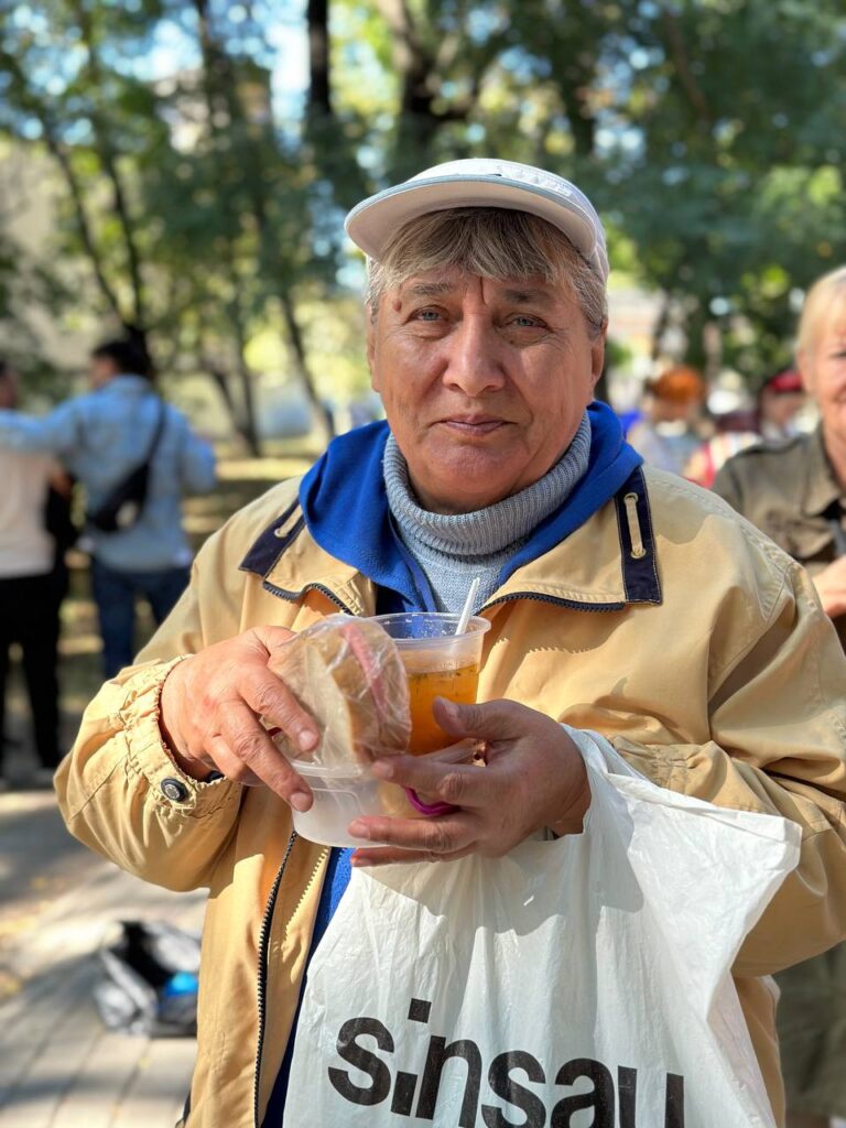 elderly person holding a cup of warm soup and a sandwich