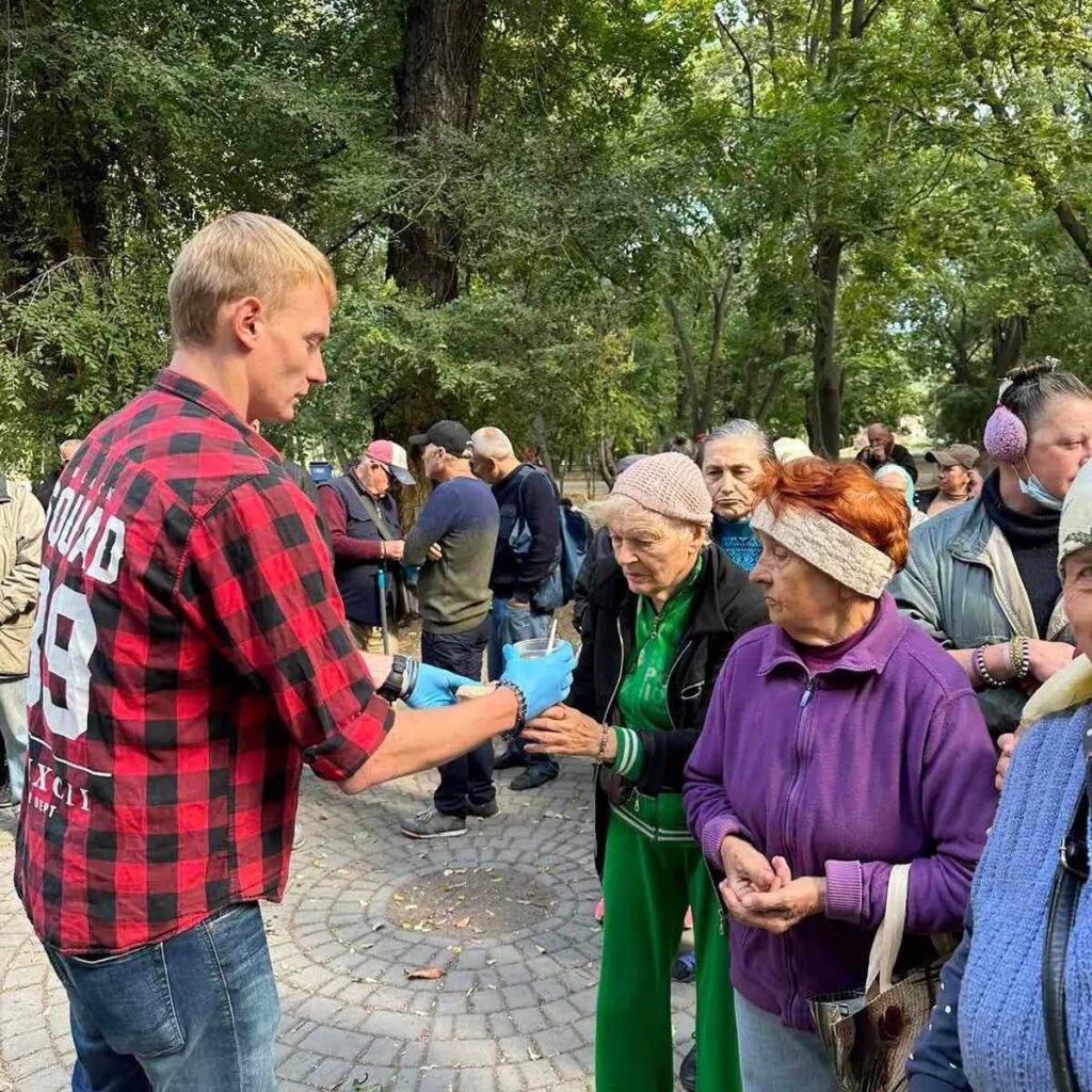 An elderly lady receiving a cup of soup surrounded by a group of people
