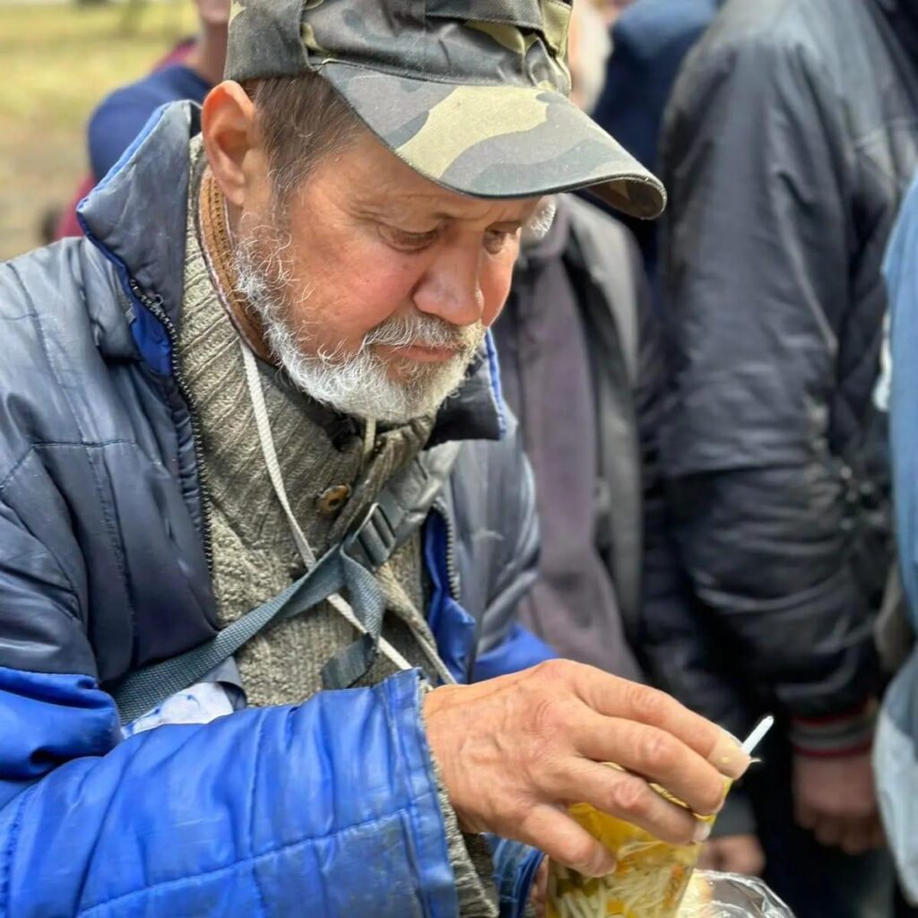 An elderly man holding a cup of soup