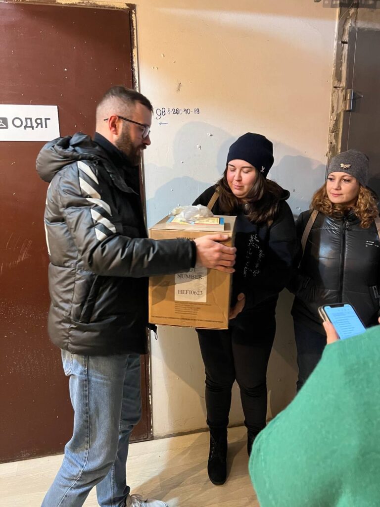 Man handing box to two women in dark clothes and warm hats