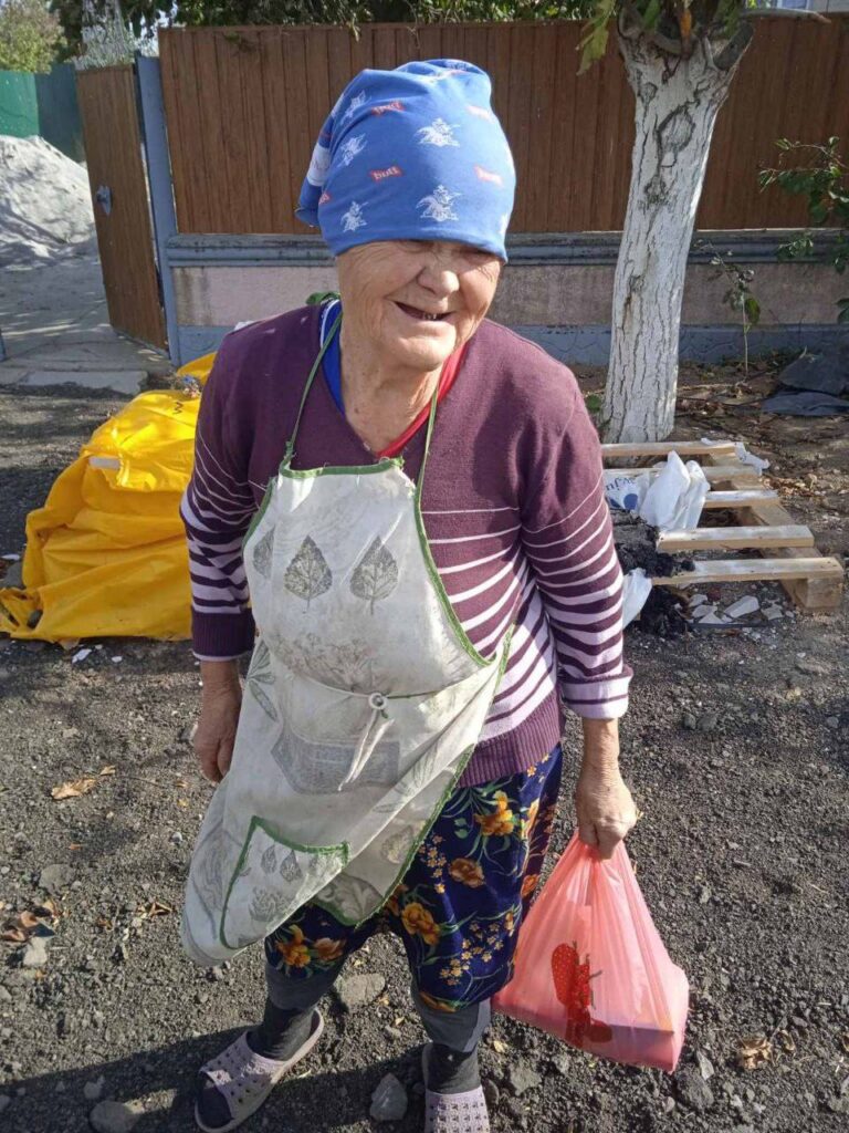An elderly woman with a kind smile holding a bag of items