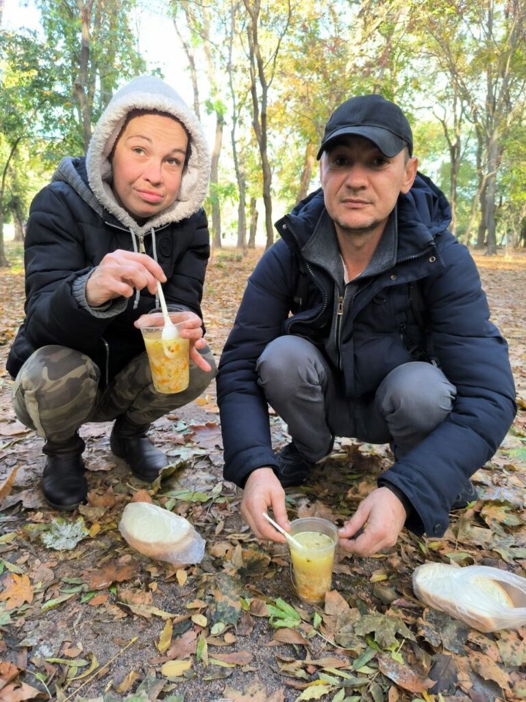 Man and woman eating soup in a forest.