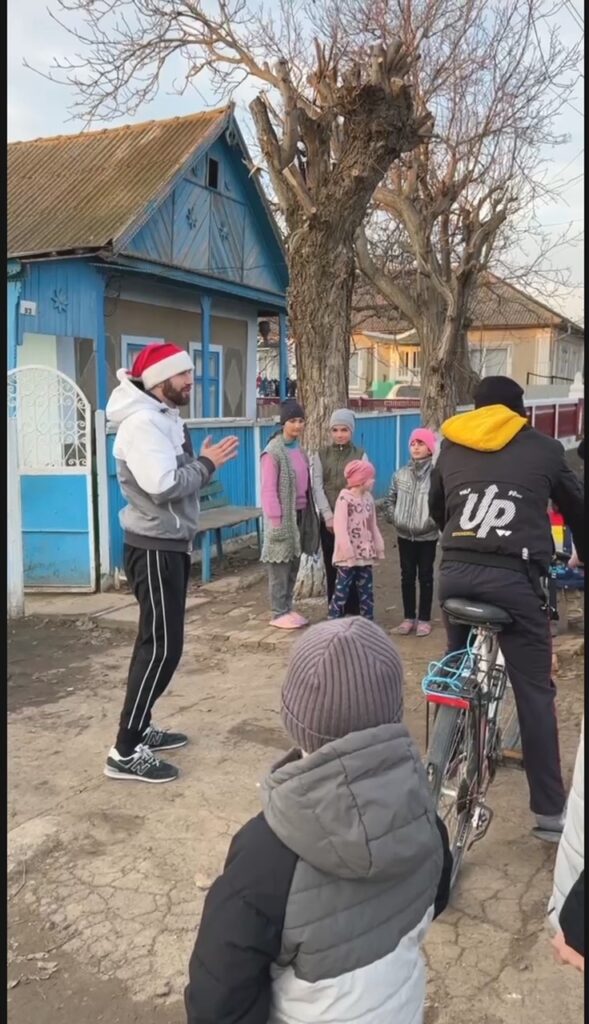 Man in a Santa Claus hat with kids gathered around him.