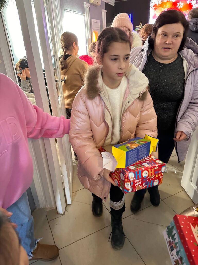 Young girl holding gifts from outreach alongside adult woman
