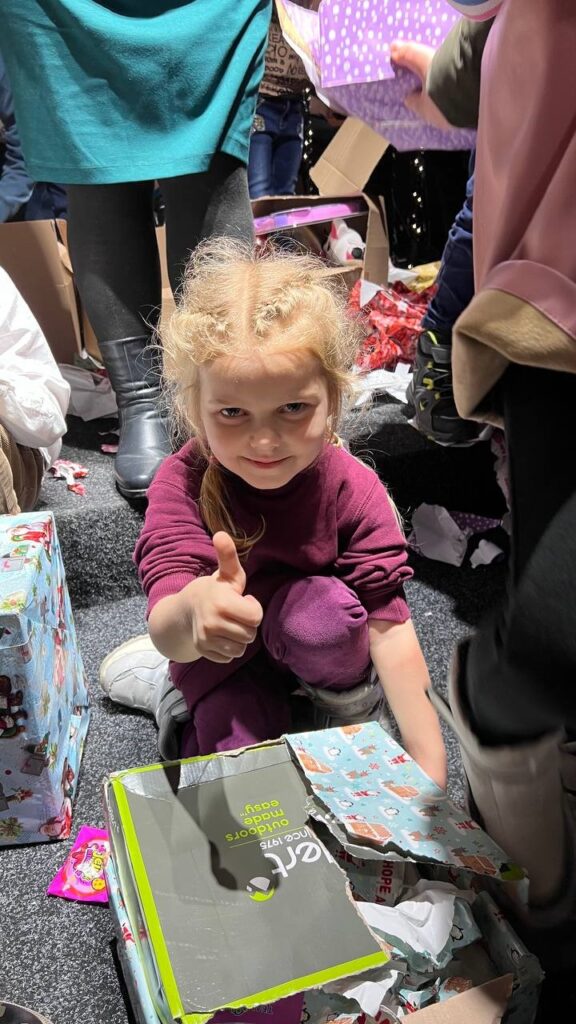 Little girl gives a thumbs up as she opens a gift.