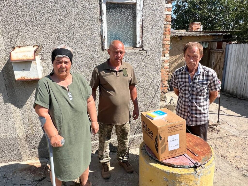 Two men and one woman with a box of food on a table in the center.