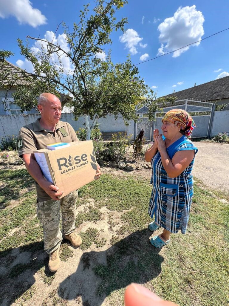 Man with a box of food and a woman nearby outside.