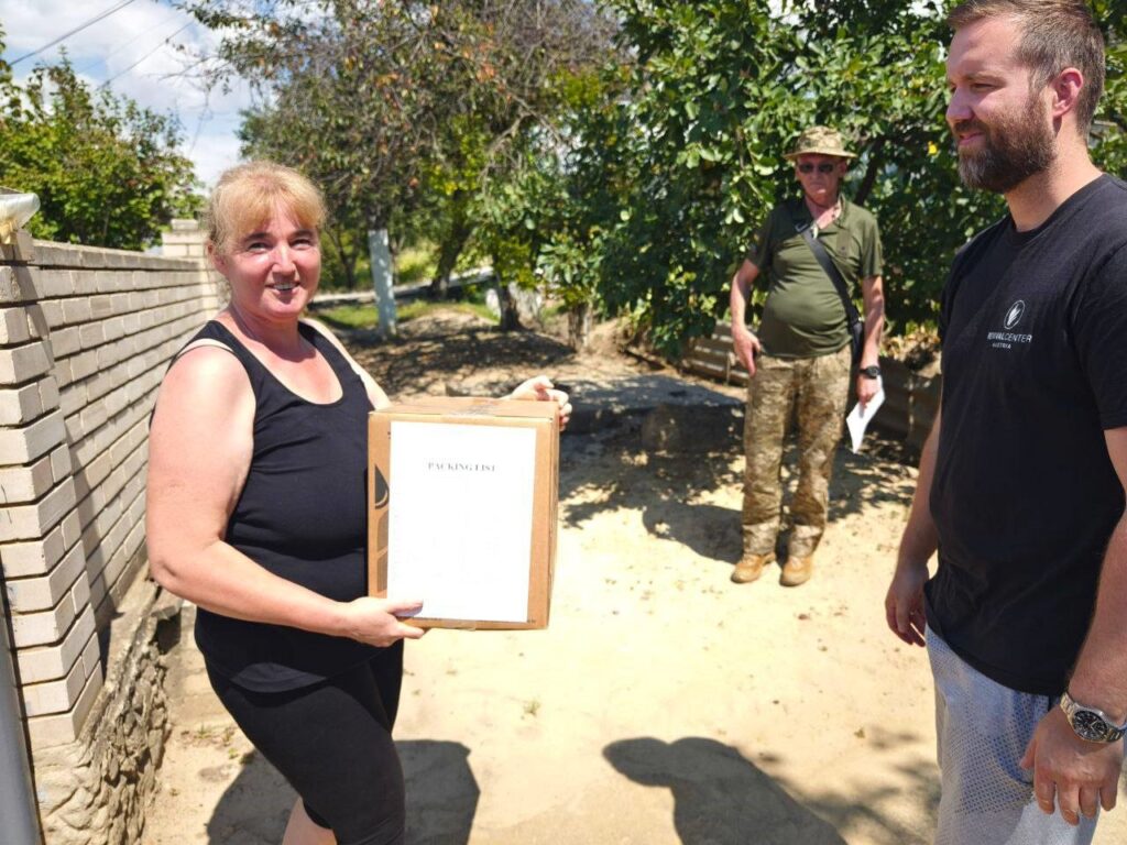 Woman with a package in her hands and smiling with two other men nearby.